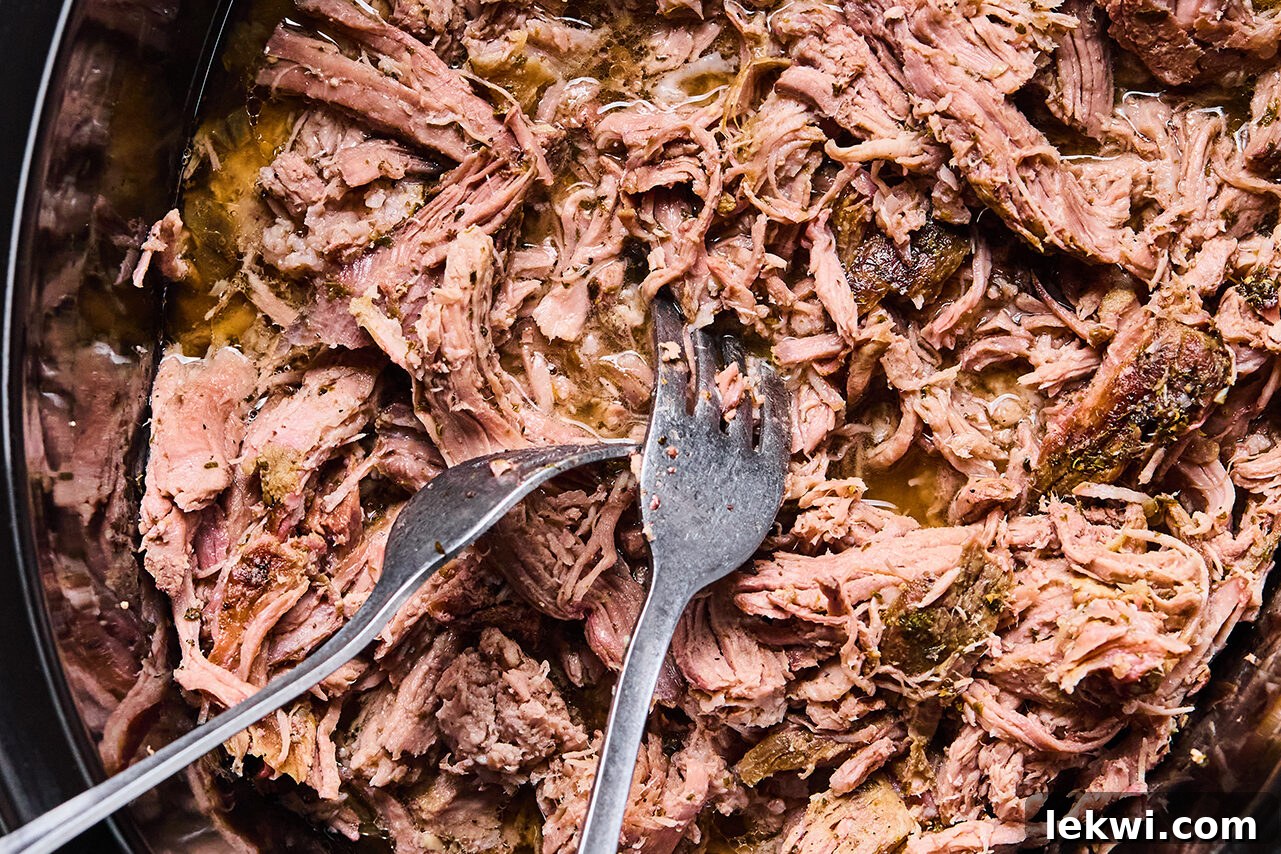 Shredded carnitas in a slow cooker with two forks. 