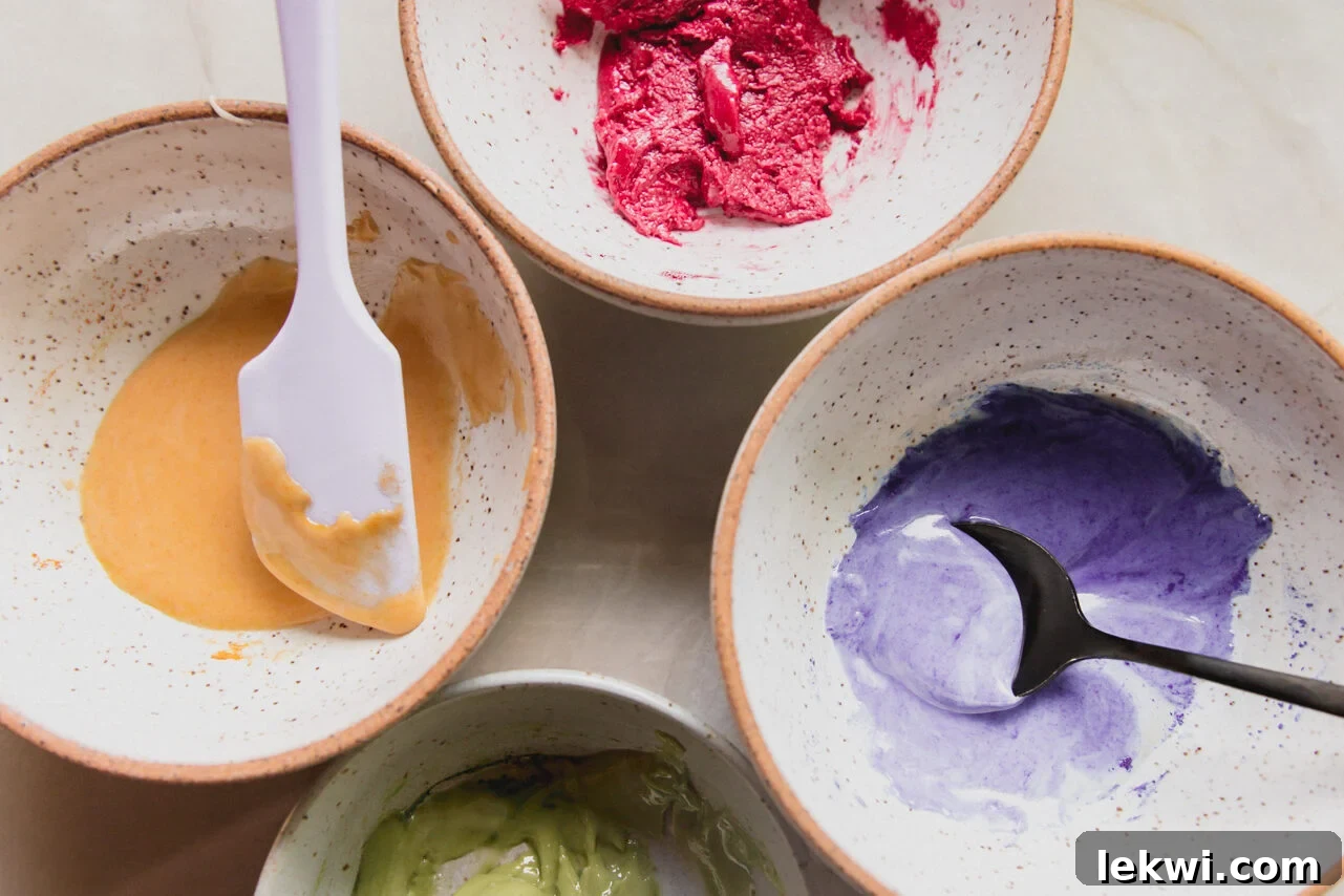 Four separate bowls, each containing a portion of the thick icing, now vibrantly dyed with natural food colorings.