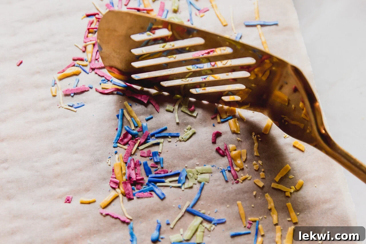 A spatula gently breaking up the hardened, dried lines of icing into individual, classic sprinkle pieces.