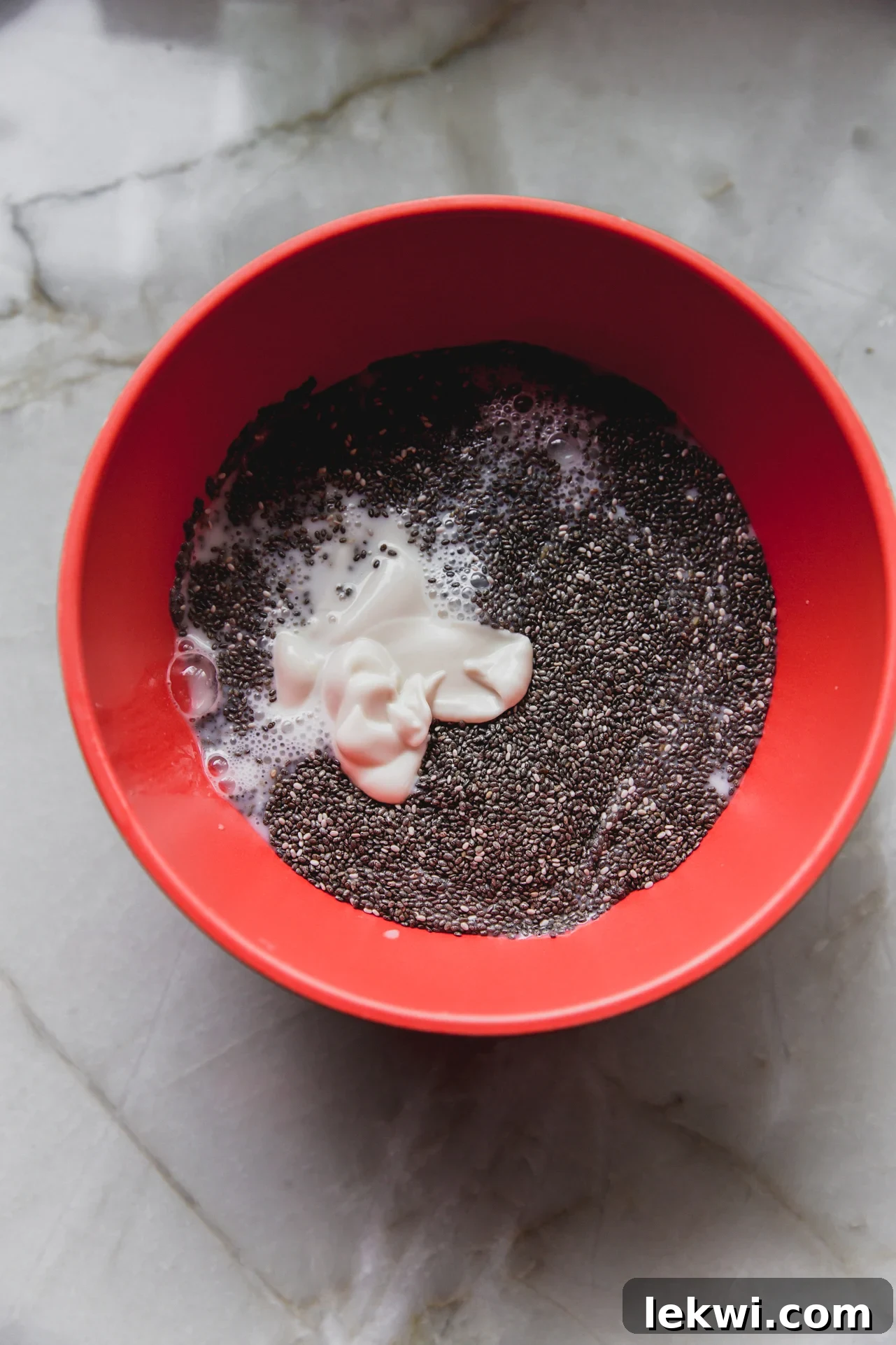 A medium bowl containing chia seeds, almond milk, vanilla coconut yogurt, and maple syrup before being mixed.