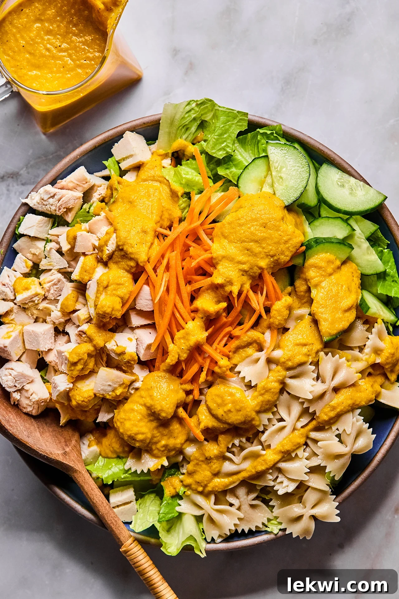 A large salad bowl with the mixed ingredients being drizzled with Japanese Ginger Dressing.