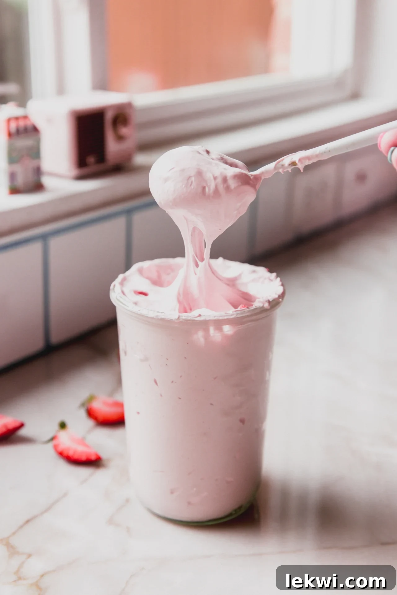 Strawberry marshmallow fluff in a glass jar with a spoon dipping in.