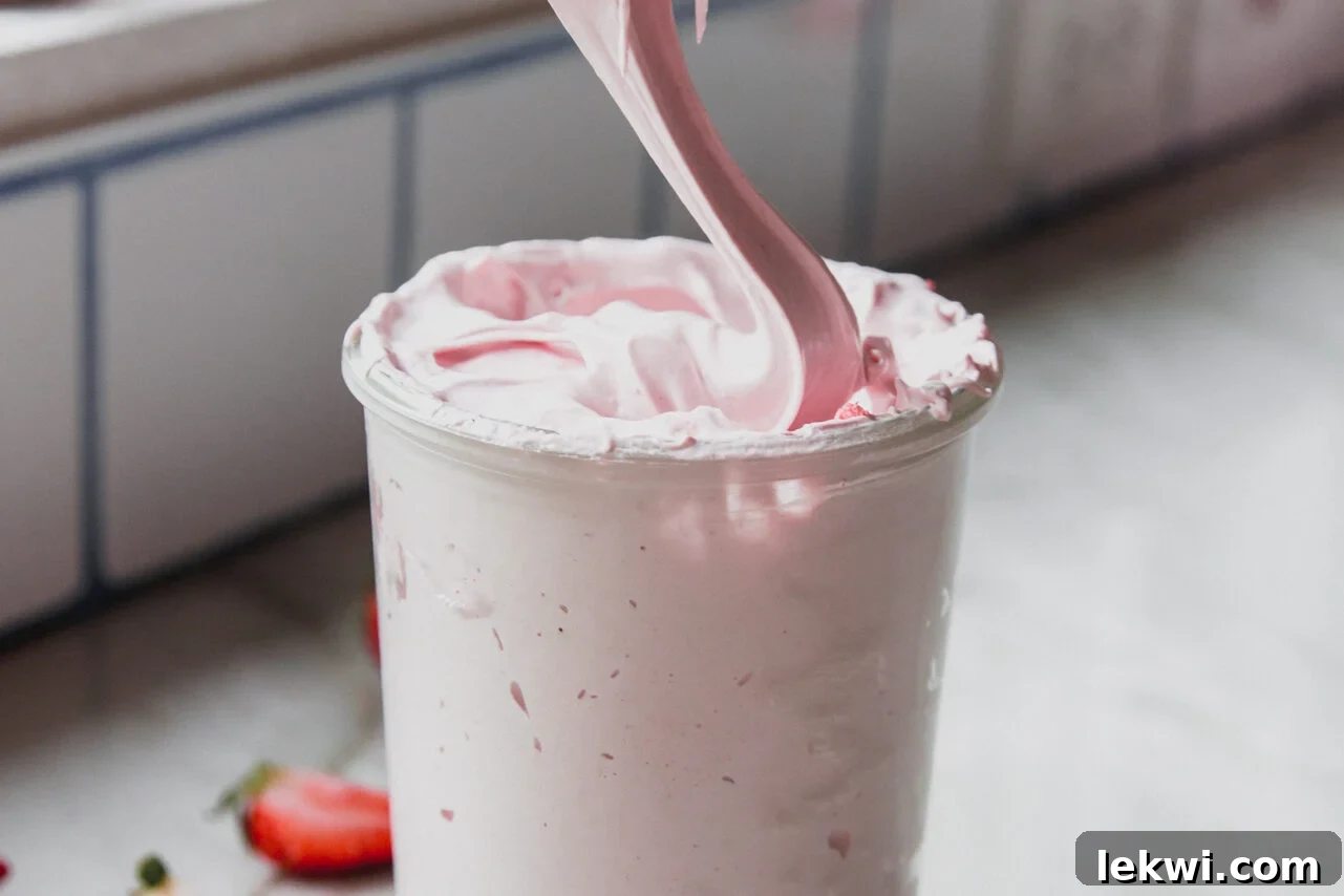 Pouring strawberry marshmallow fluff into a jar.