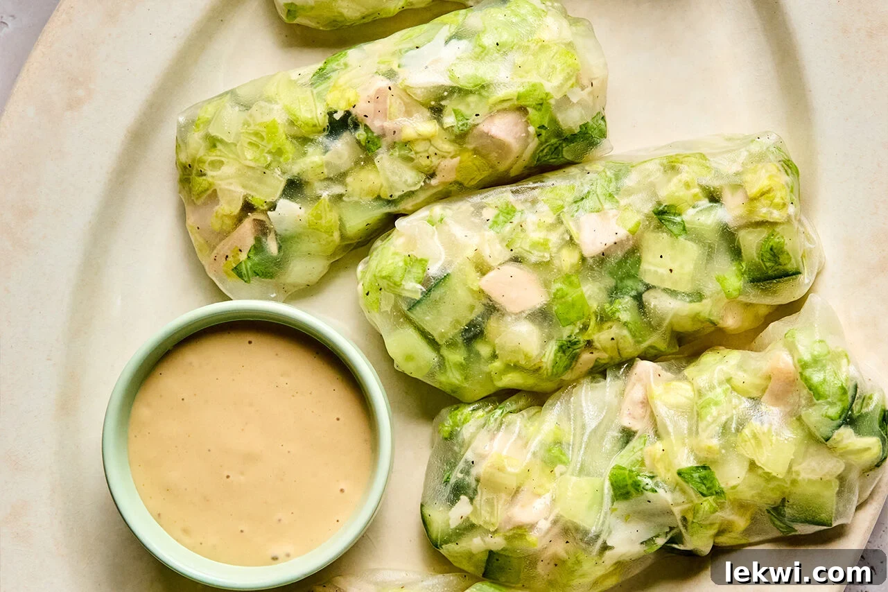 A beautiful platter showcasing several finished chicken Caesar salad rice paper rolls, artfully arranged and accompanied by a small bowl of extra creamy Caesar dressing for dipping.