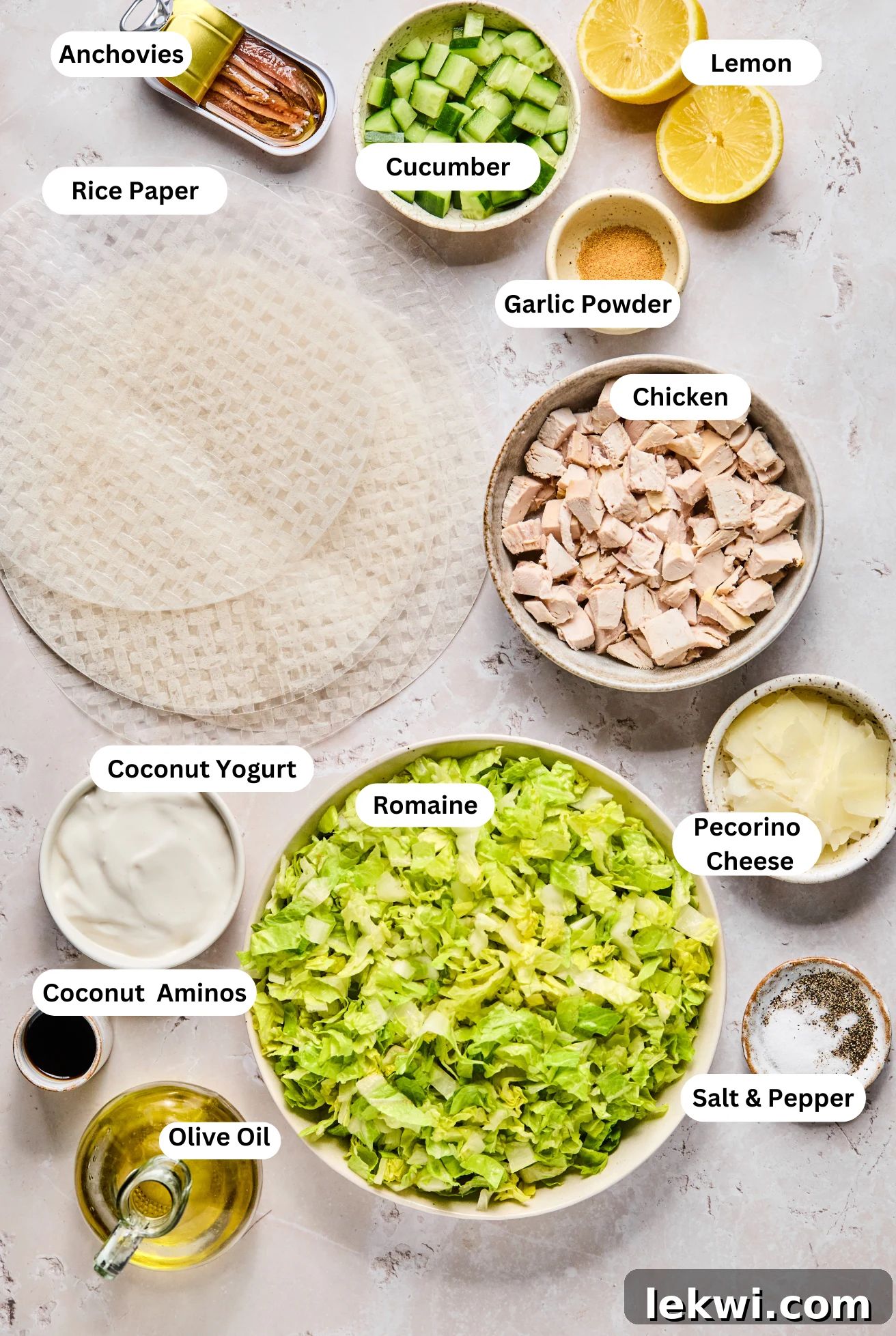 All the fresh ingredients for homemade chicken Caesar rice paper rolls carefully laid out on a table, including cooked chicken, crisp romaine lettuce, diced cucumber, and various dressing components.