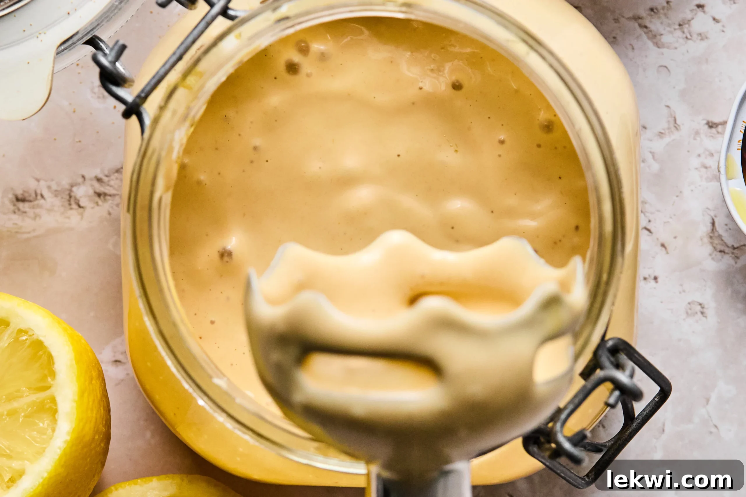 An immersion blender actively blending the Caesar dressing ingredients in a jar, working to create a smooth, creamy emulsion.