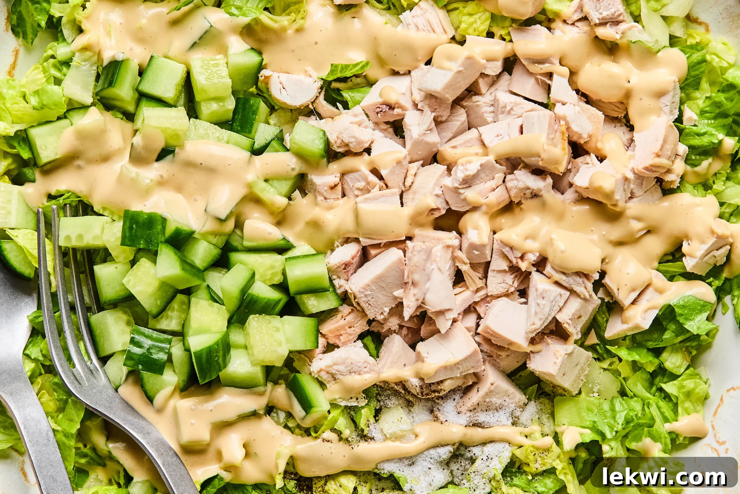 The chicken Caesar salad mixture with a generous amount of homemade dressing freshly poured over it, prior to being mixed.