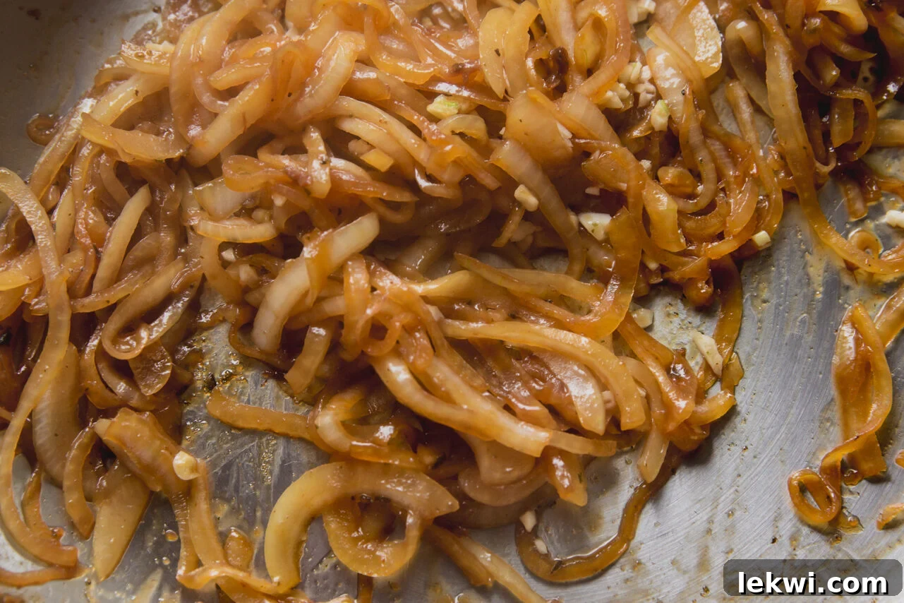 Sliced onions and shallots softening in the pan with coconut aminos.