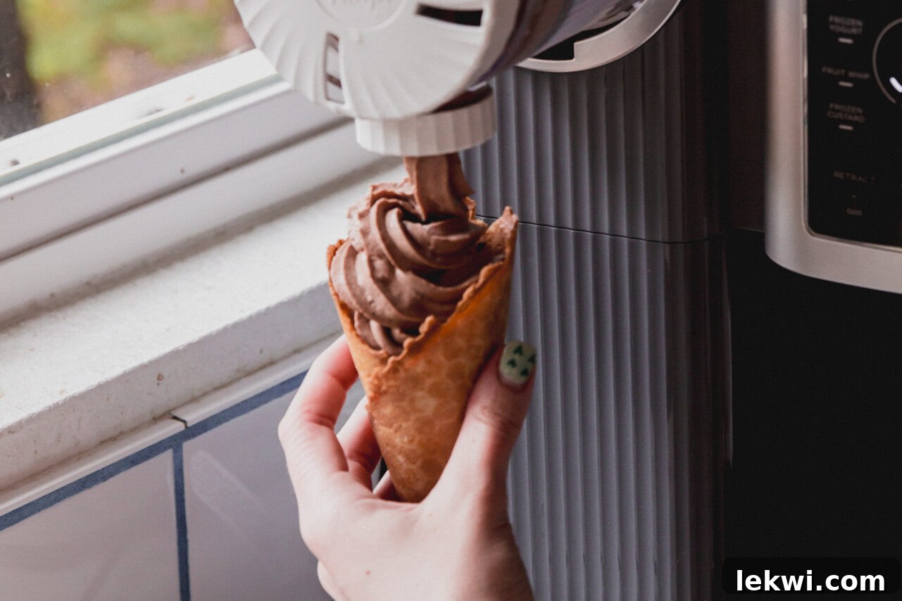 The Ninja Creami swirl attachment dispensing chocolate protein ice cream into a cone.