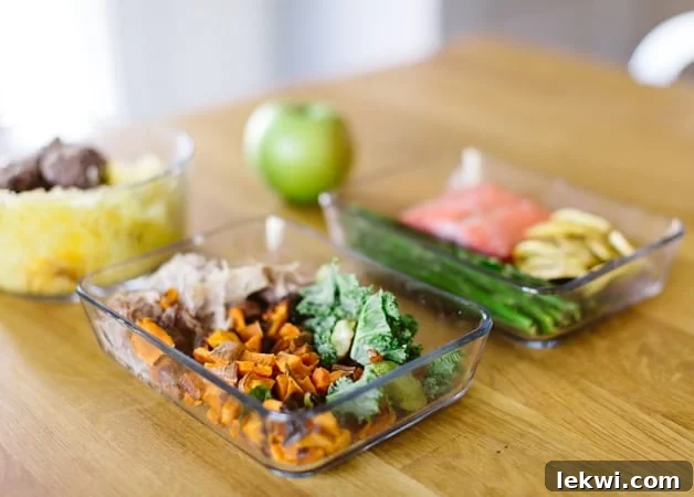 A table with two containers of meal prep and an apple on it.