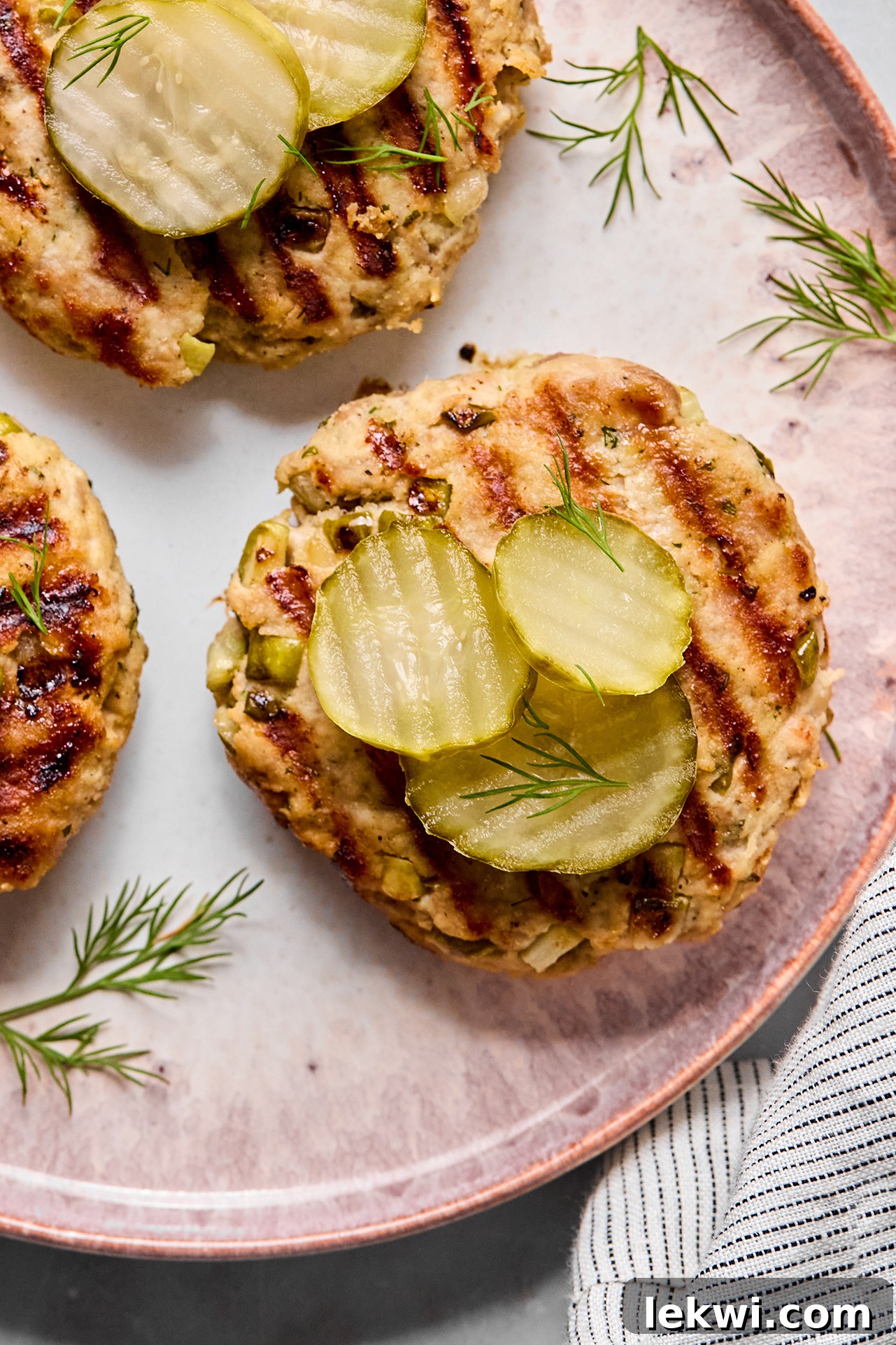 Juicy ground chicken burgers topped with fresh pickles on a serving platter, ready for a summer meal.