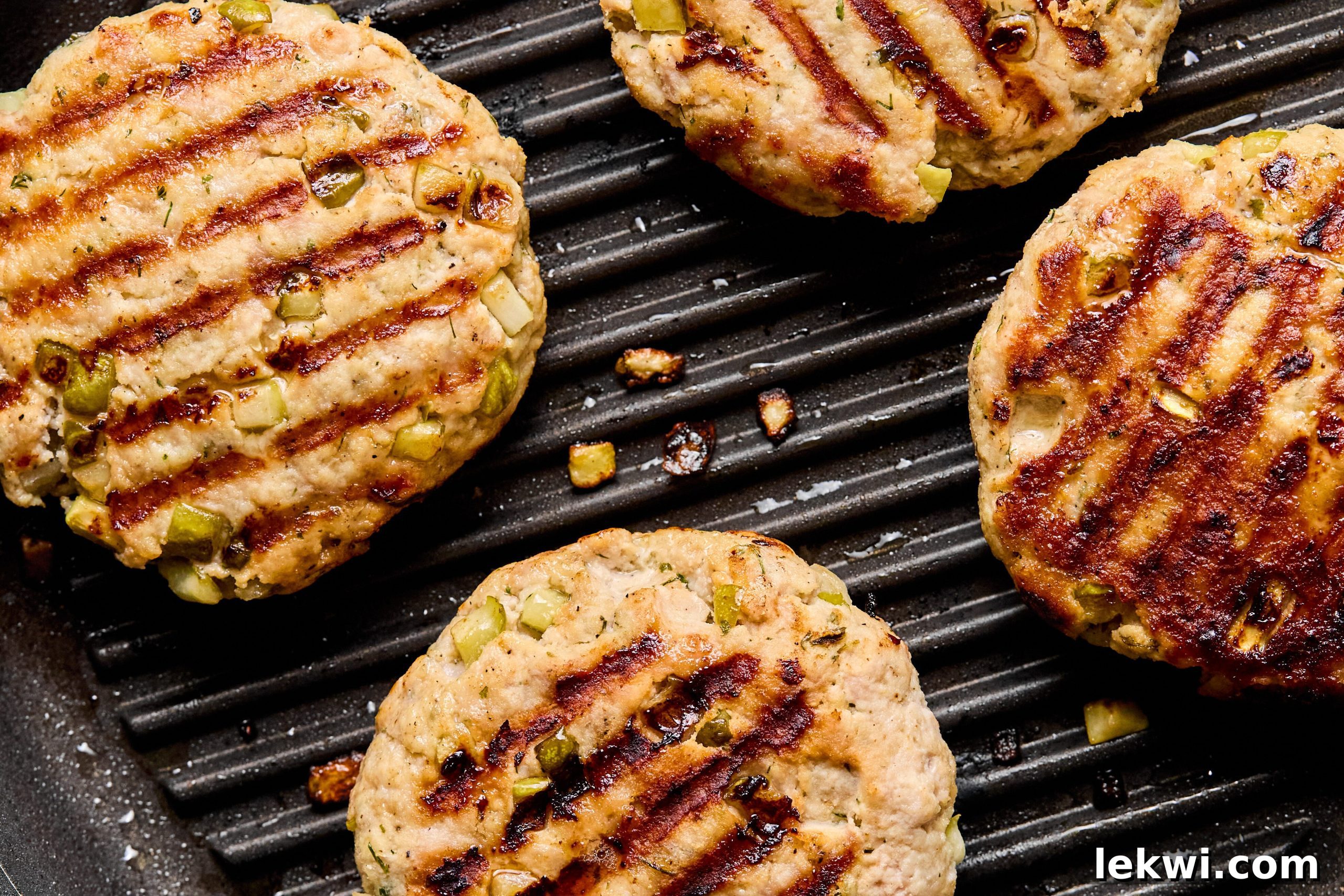 Four perfectly grilled ground chicken burgers showing appealing grill marks on a hot grill pan.