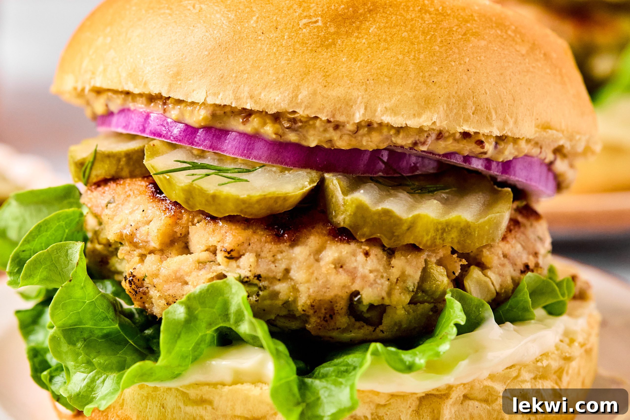 A fully assembled ground chicken pickle burger on a gluten-free bun, layered with lettuce, dill, pickle slices, and red onion.