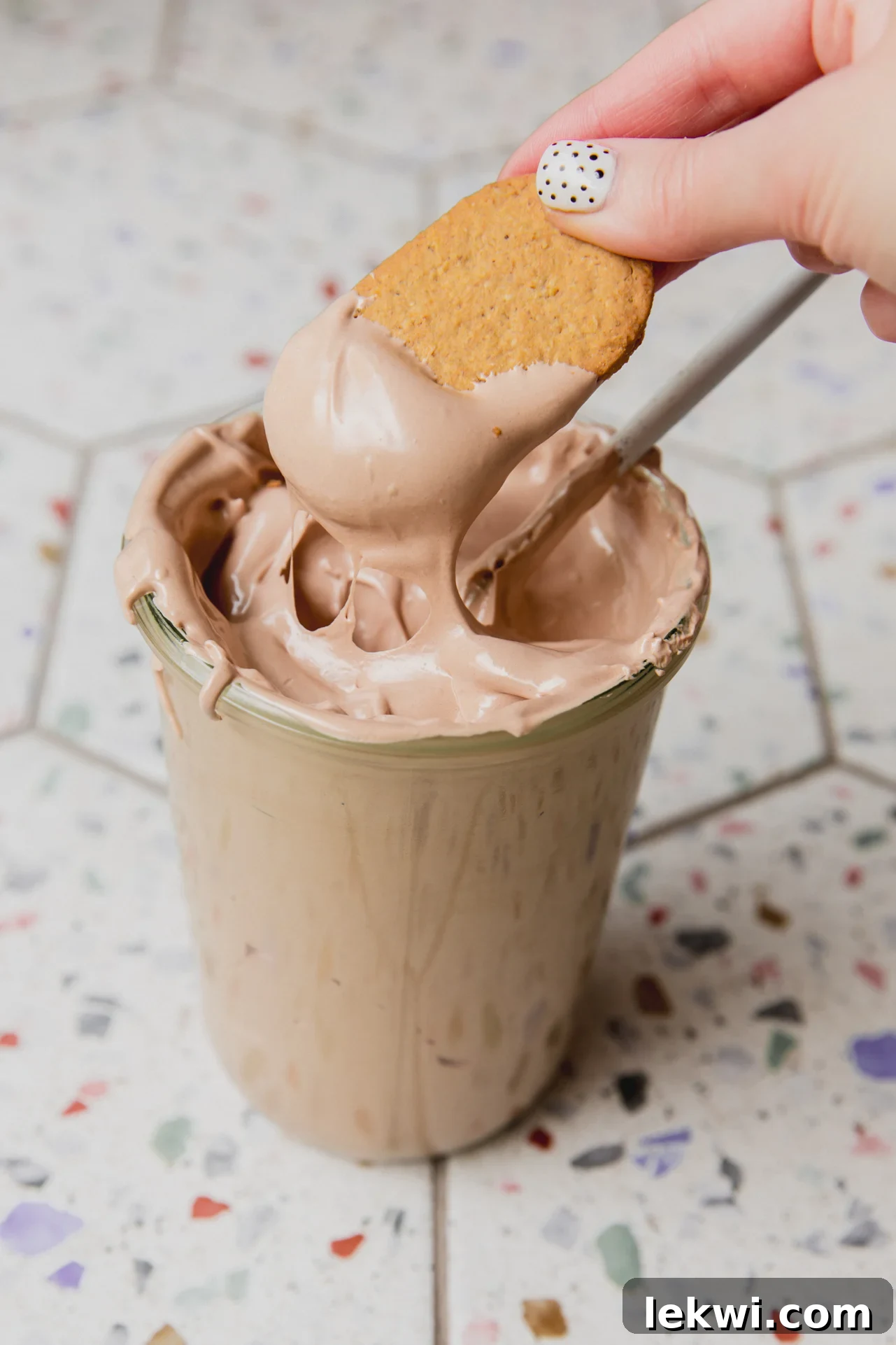 Chocolate espresso marshmallow fluff in a large glass jar with a graham cracker being dipped in.