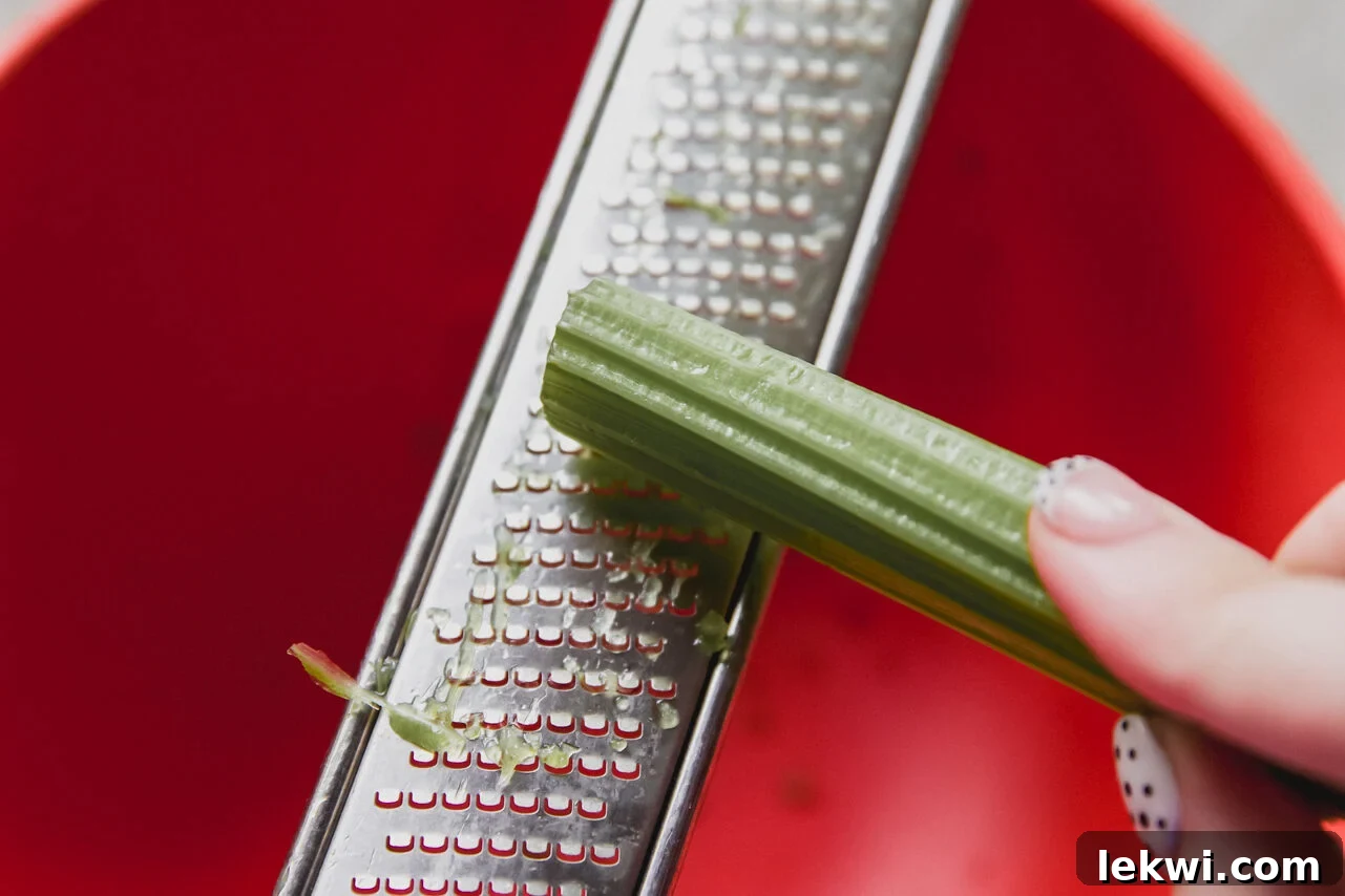 A microplane being used to finely shred celery directly into a bowl with chicken, demonstrating the precise preparation technique.