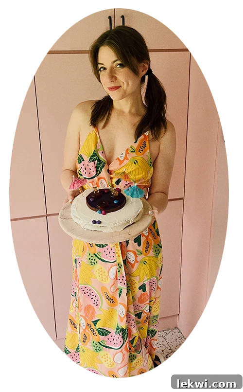 Food blogger, Michelle Hoover, smiling in a pink kitchen while holding a beautiful swimming pool cake on a plate.