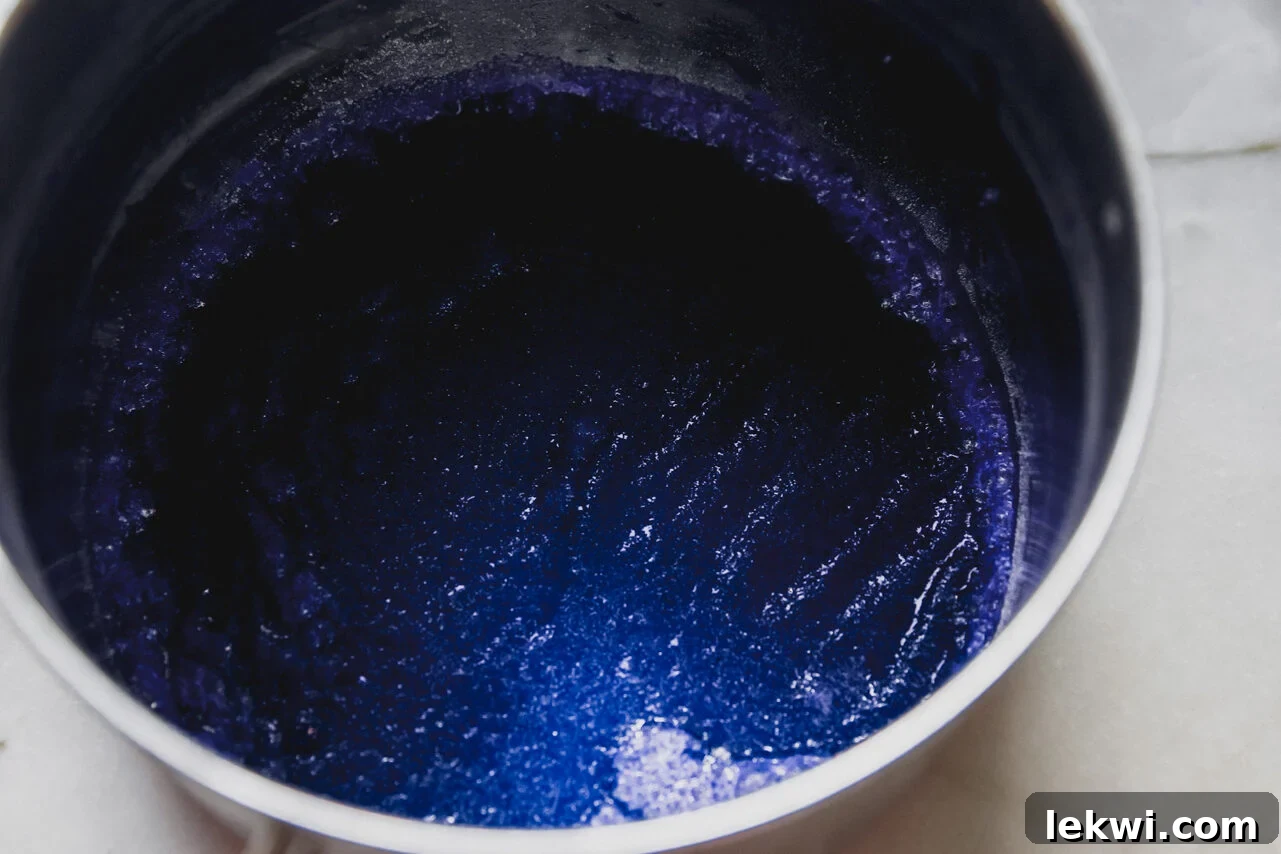 Apple juice, gelatin, and blue spirulina combined in a pot on a stovetop.