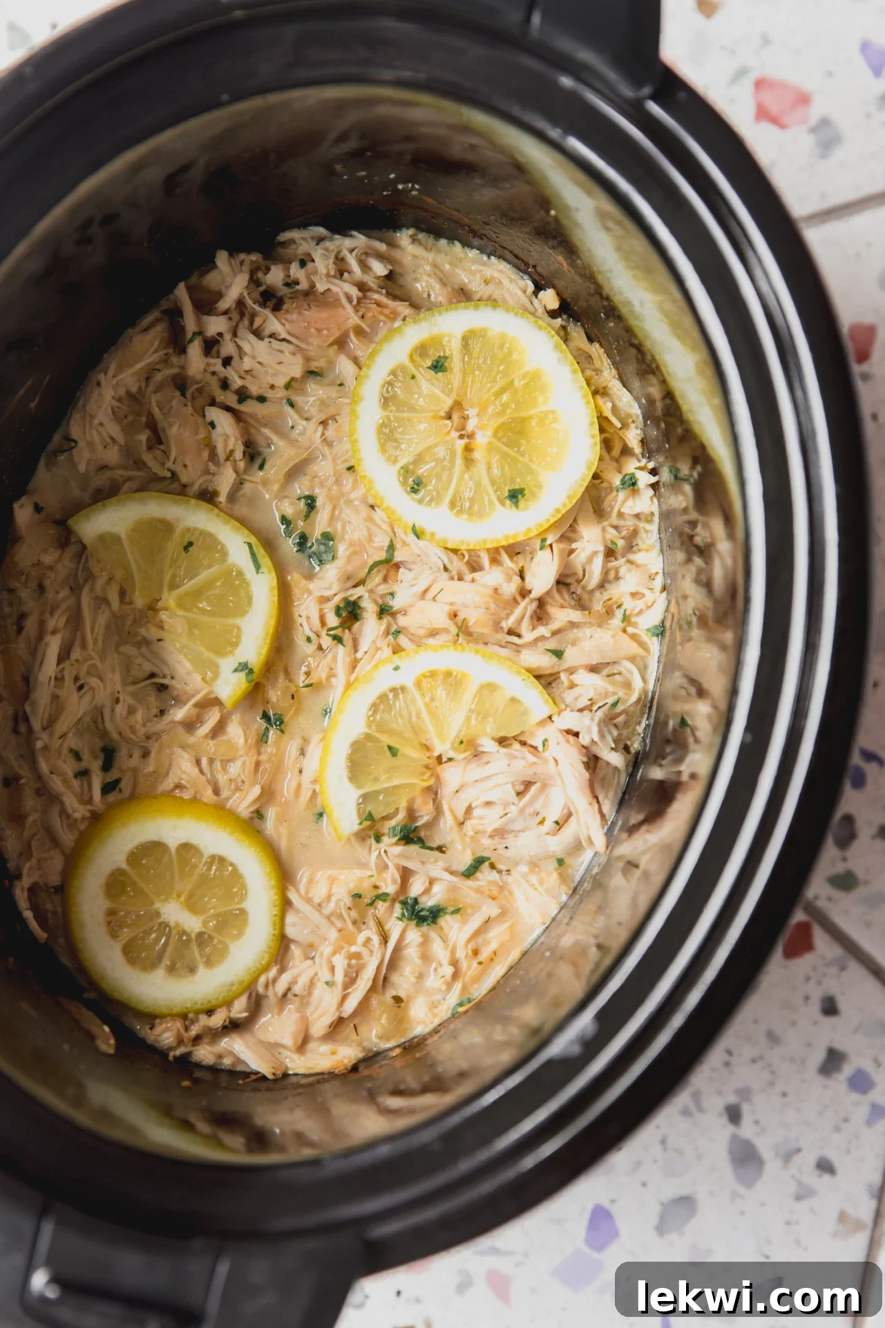 Slow cooker Greek chicken in the slow cooker topped with lemon slices, ready to be shredded.