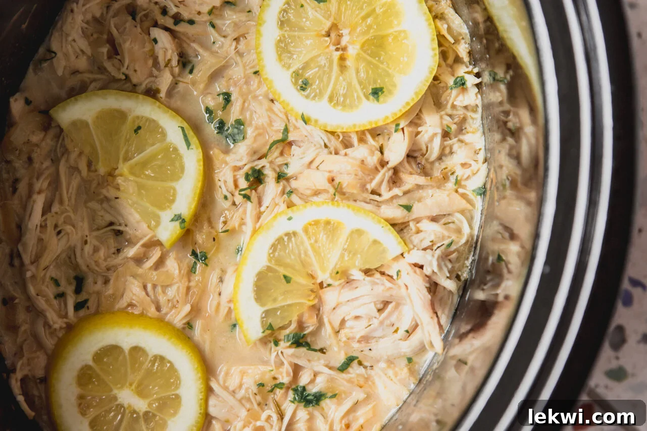 Slow cooker Greek chicken cooking in the slow cooker with lemon slices on top.