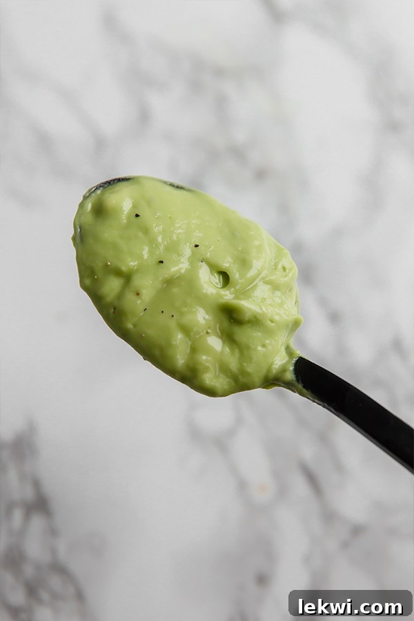 A spoon delicately holding a scoop of smooth, green avocado dressing, showcasing its creamy texture.