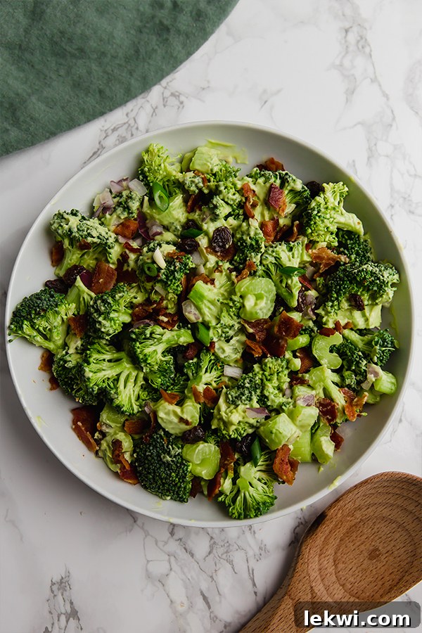 A beautiful white bowl filled generously with a fresh and creamy avocado bacon broccoli salad.