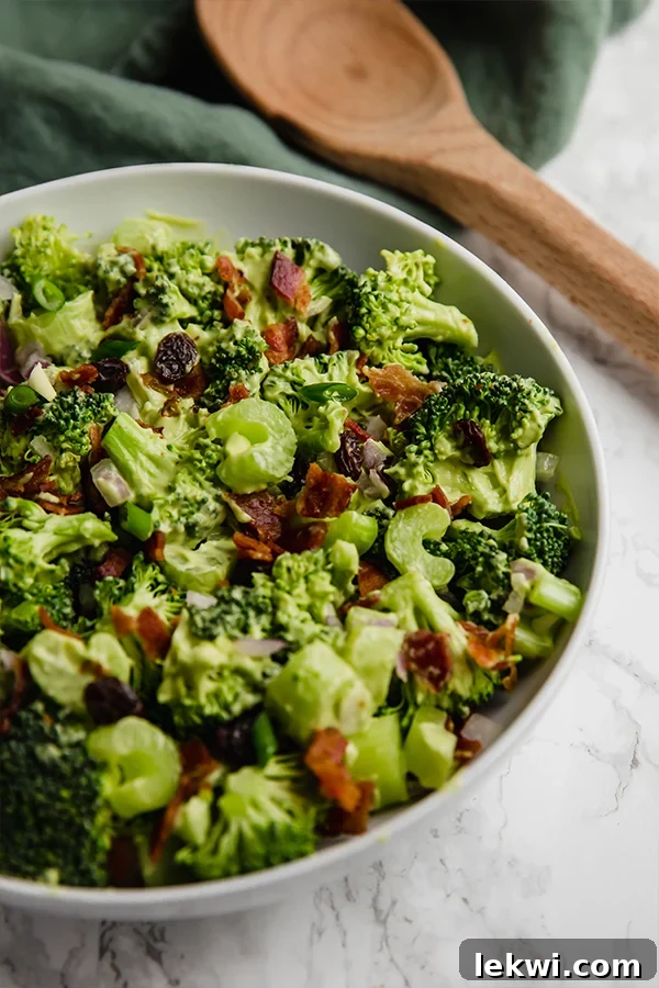 A white bowl filled with avocado bacon broccoli salad, garnished with fresh herbs.