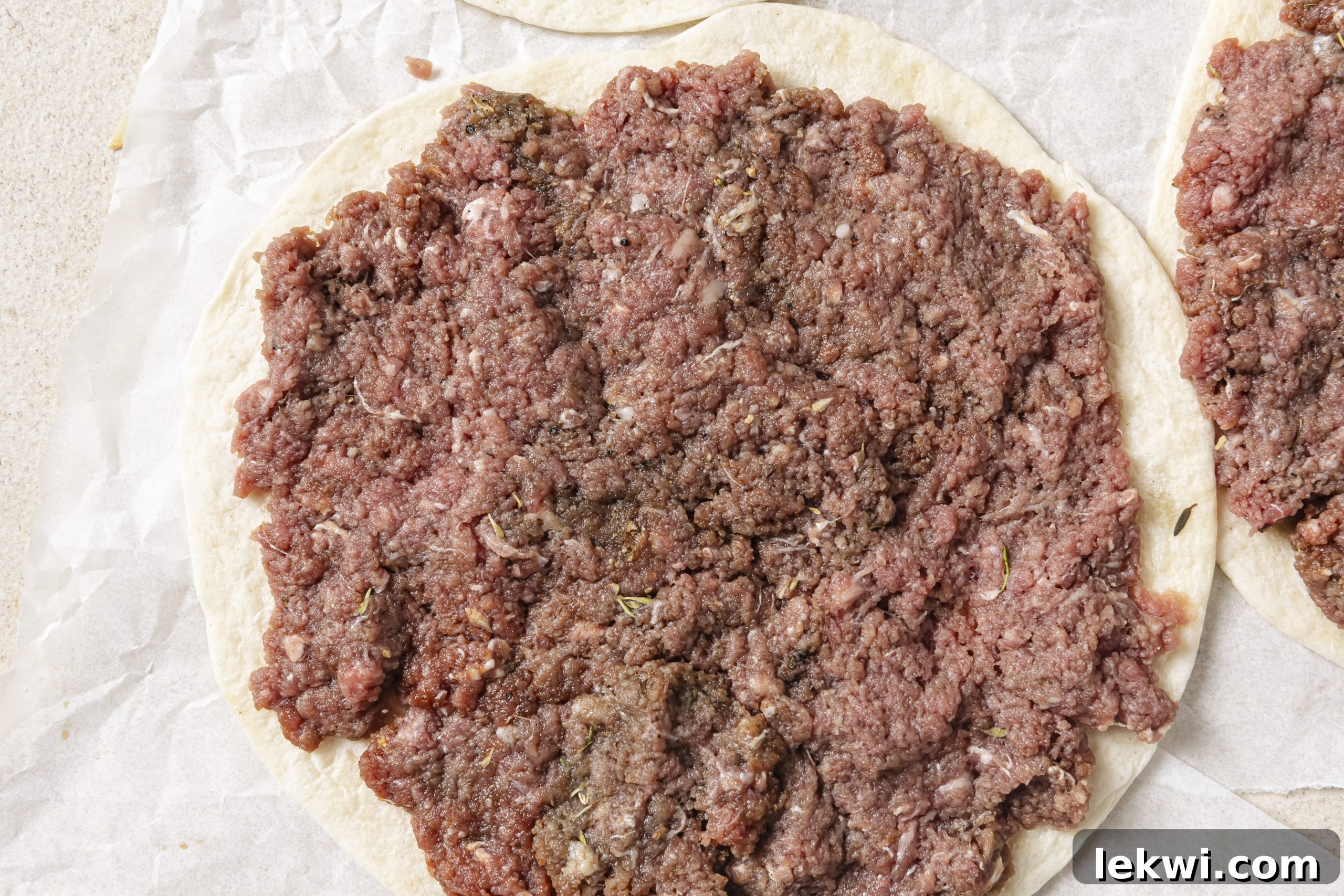 A tortilla with a thin, even layer of ground beef pressed onto its surface, ready for cooking.