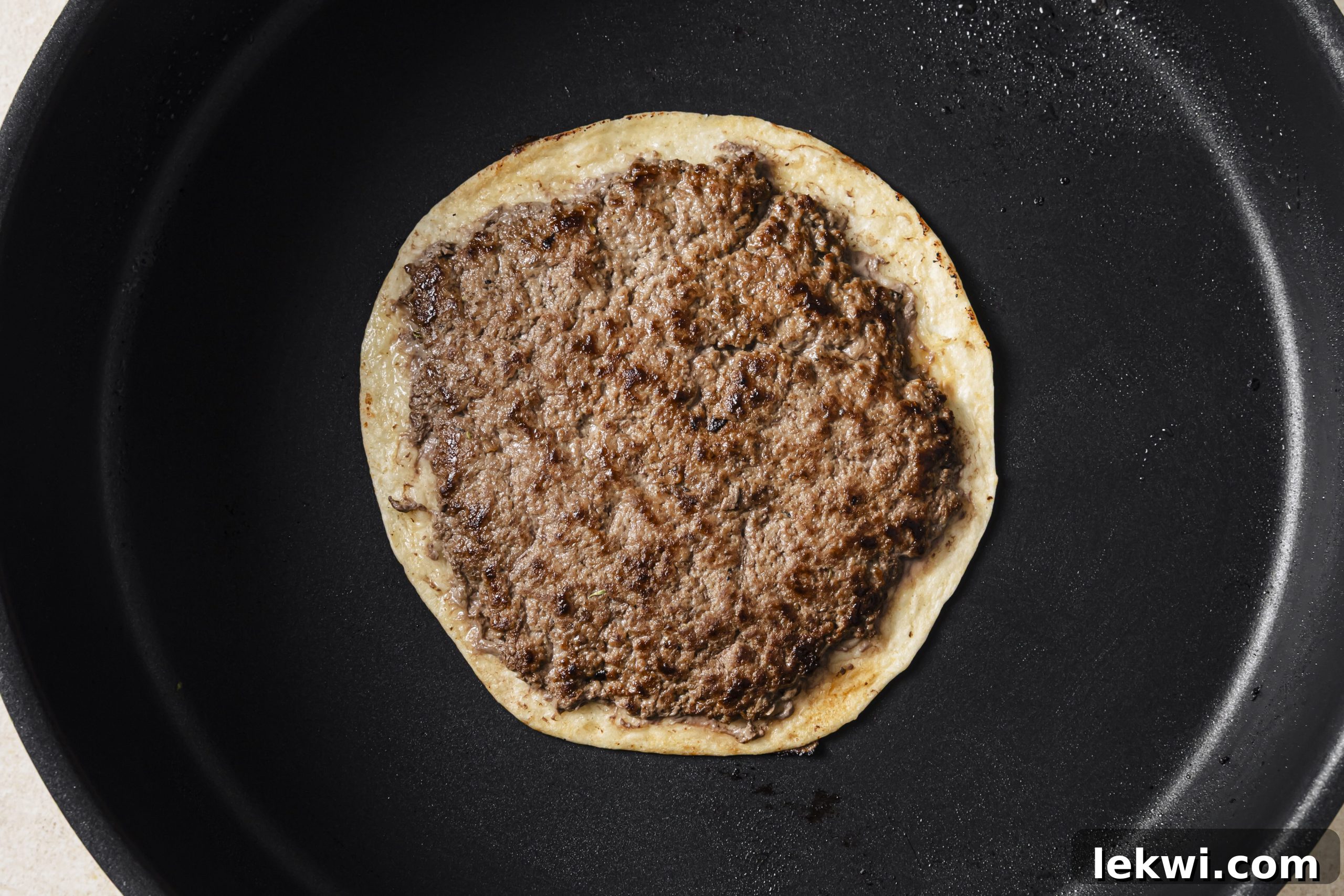 One smashburger taco cooking on a hot pan, meat-side down, developing a crispy crust.