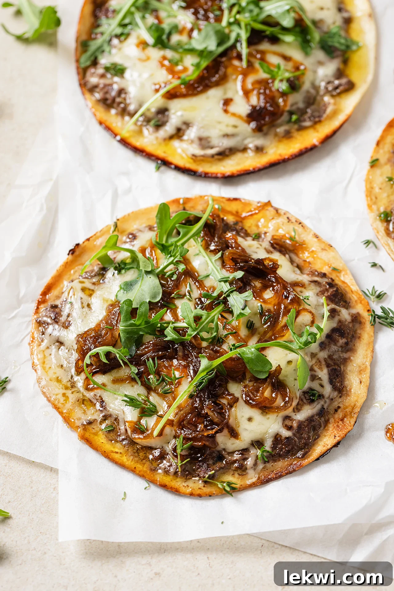 A vibrant close-up of French onion smashburger tacos, showing the golden-brown crust, melted cheese, and fresh arugula.