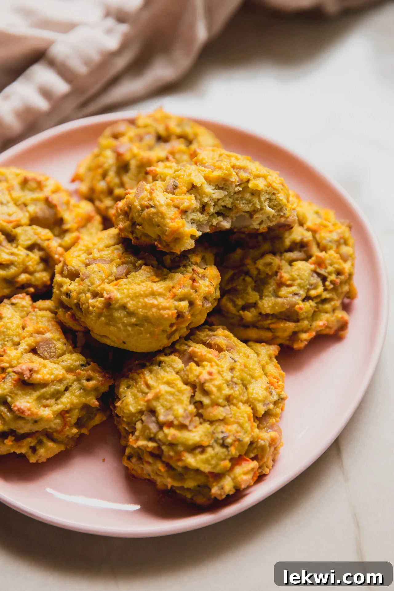 Protein breakfast sausage biscuits stacked on a pink plate with one bite taken out of one of the biscuits on top.