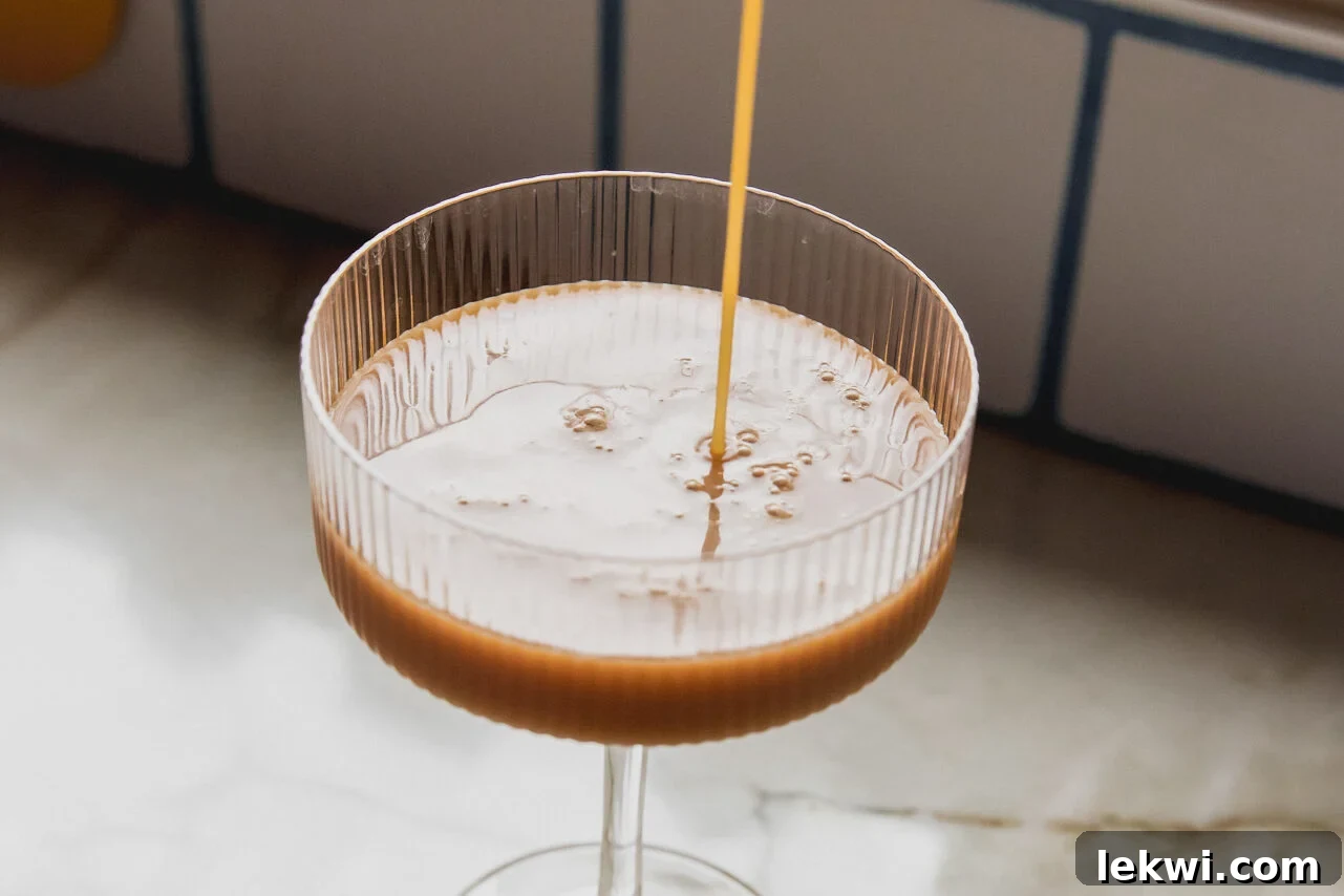 An espresso martini mocktail being carefully poured from a cocktail shaker into a chilled martini glass, showcasing its rich color and nascent foam.