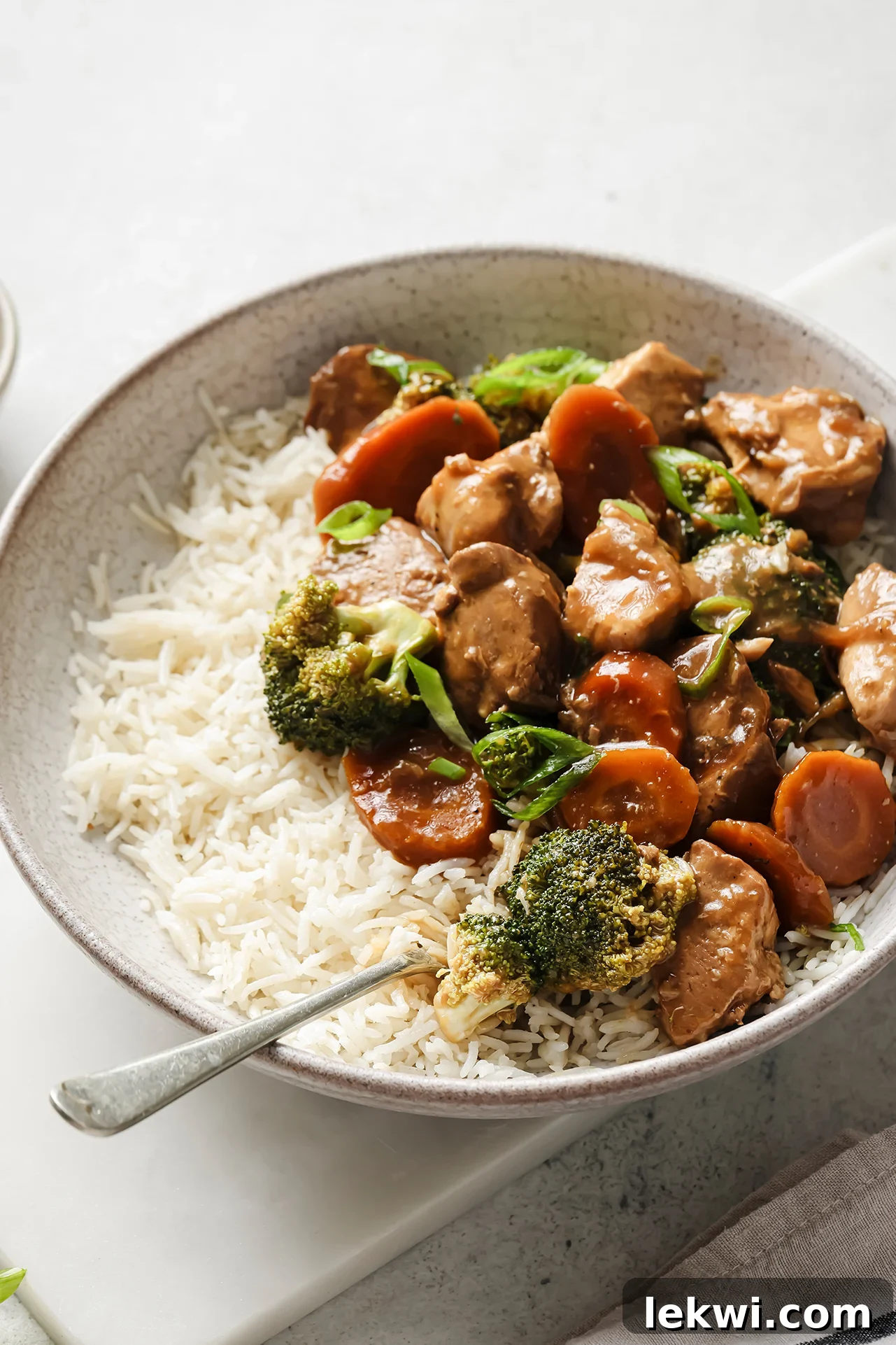 A bowl of slow cooker chicken and broccoli, served with rice and garnished with green onions.