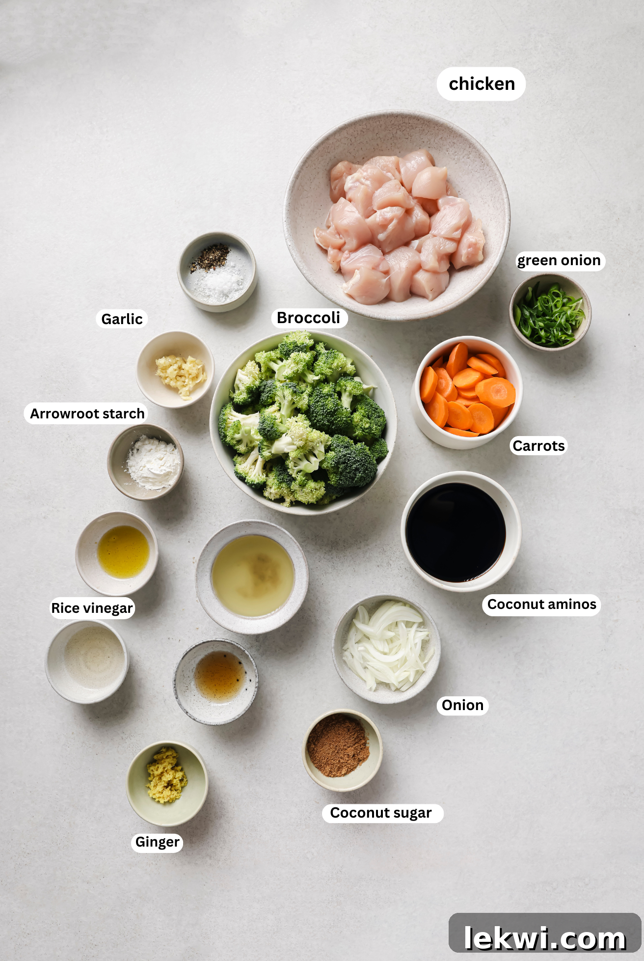 Separate bowls displaying all the ingredients required for the slow cooker chicken and broccoli recipe: chicken breast, frozen broccoli, carrots, onion, garlic, ginger, coconut aminos, coconut sugar, rice vinegar, chicken broth, arrowroot starch, and sesame oil.