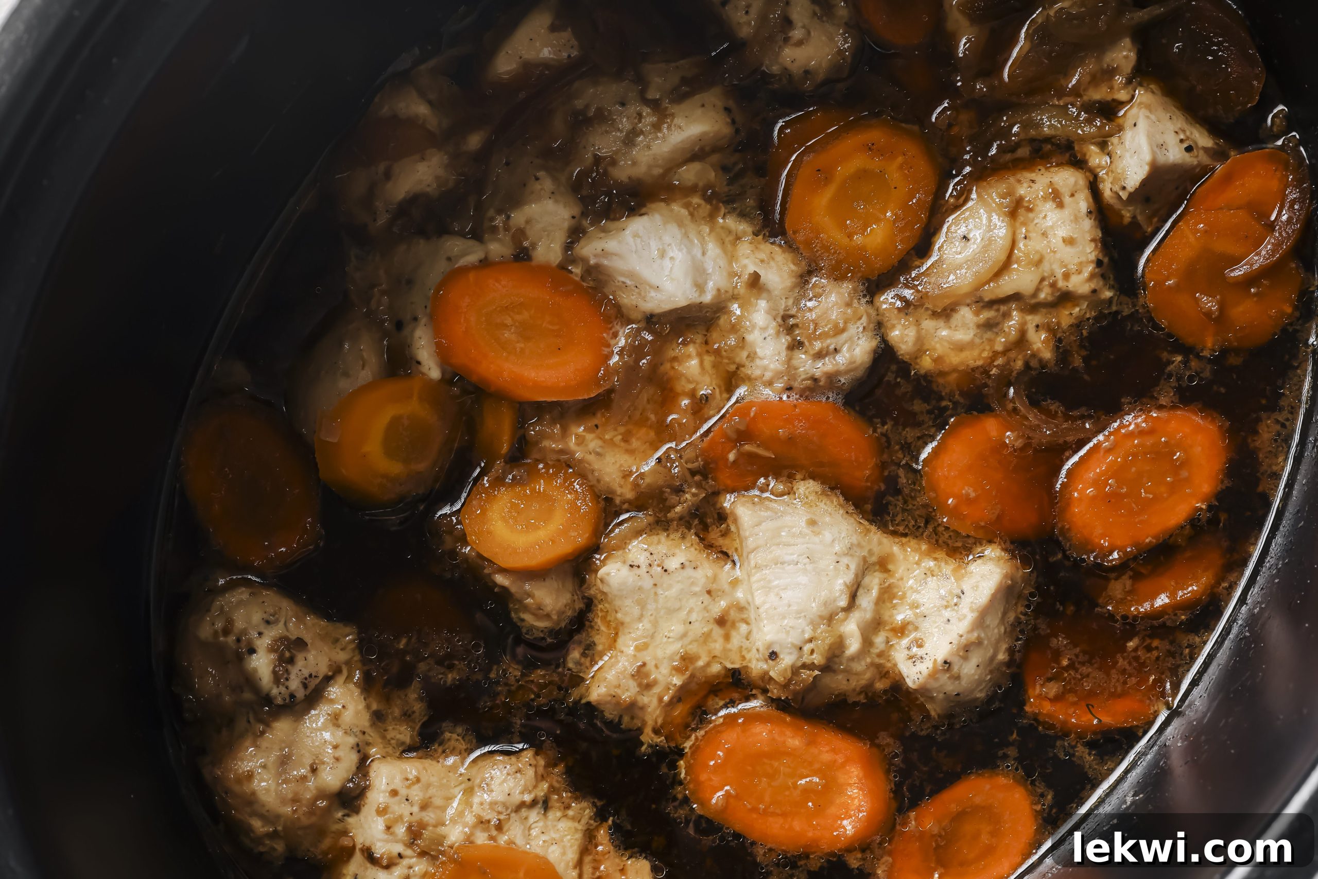 The chicken and carrots simmering in the slow cooker, submerged in the rich, savory sauce.