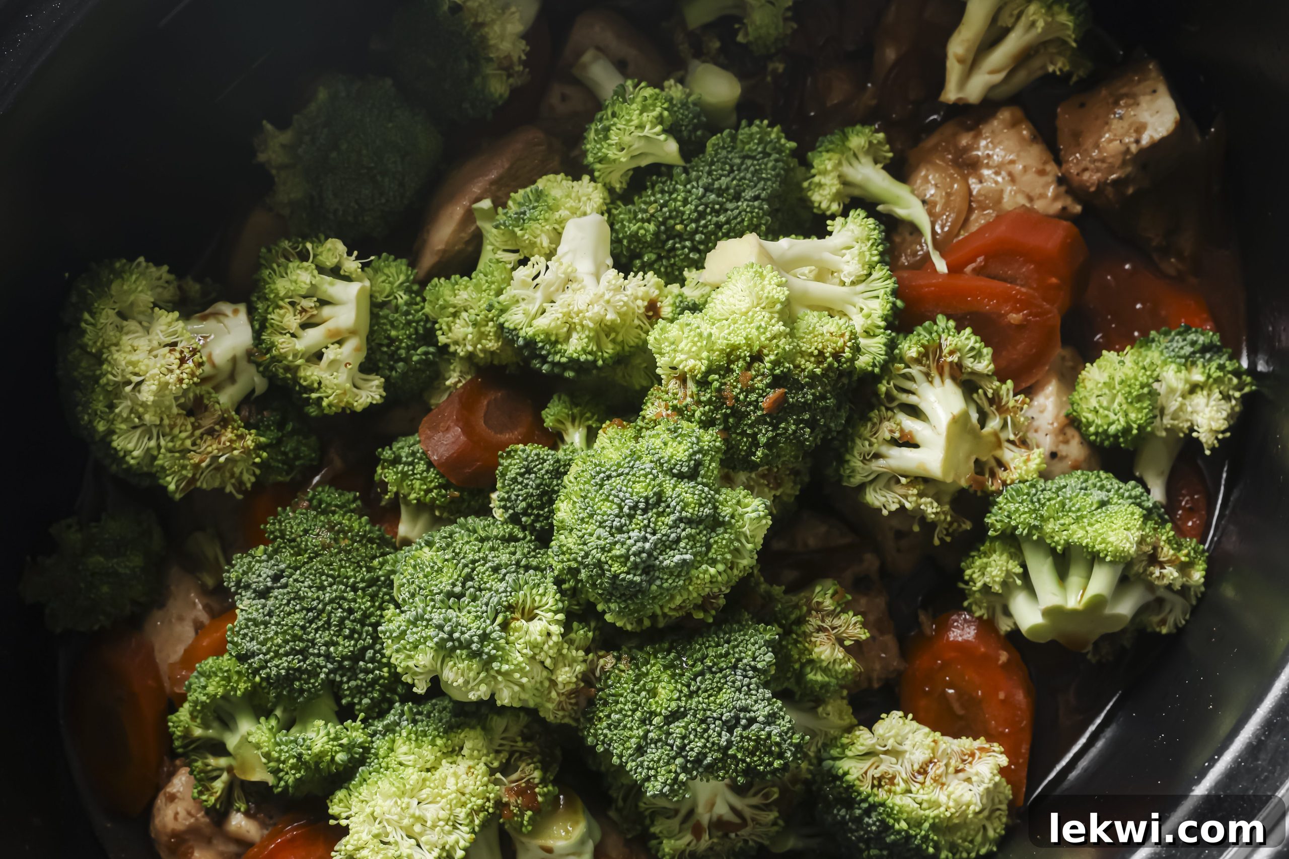 Cooked chicken and carrots in the slow cooker, with fresh broccoli florets just added on top, ready for the final cooking stage.