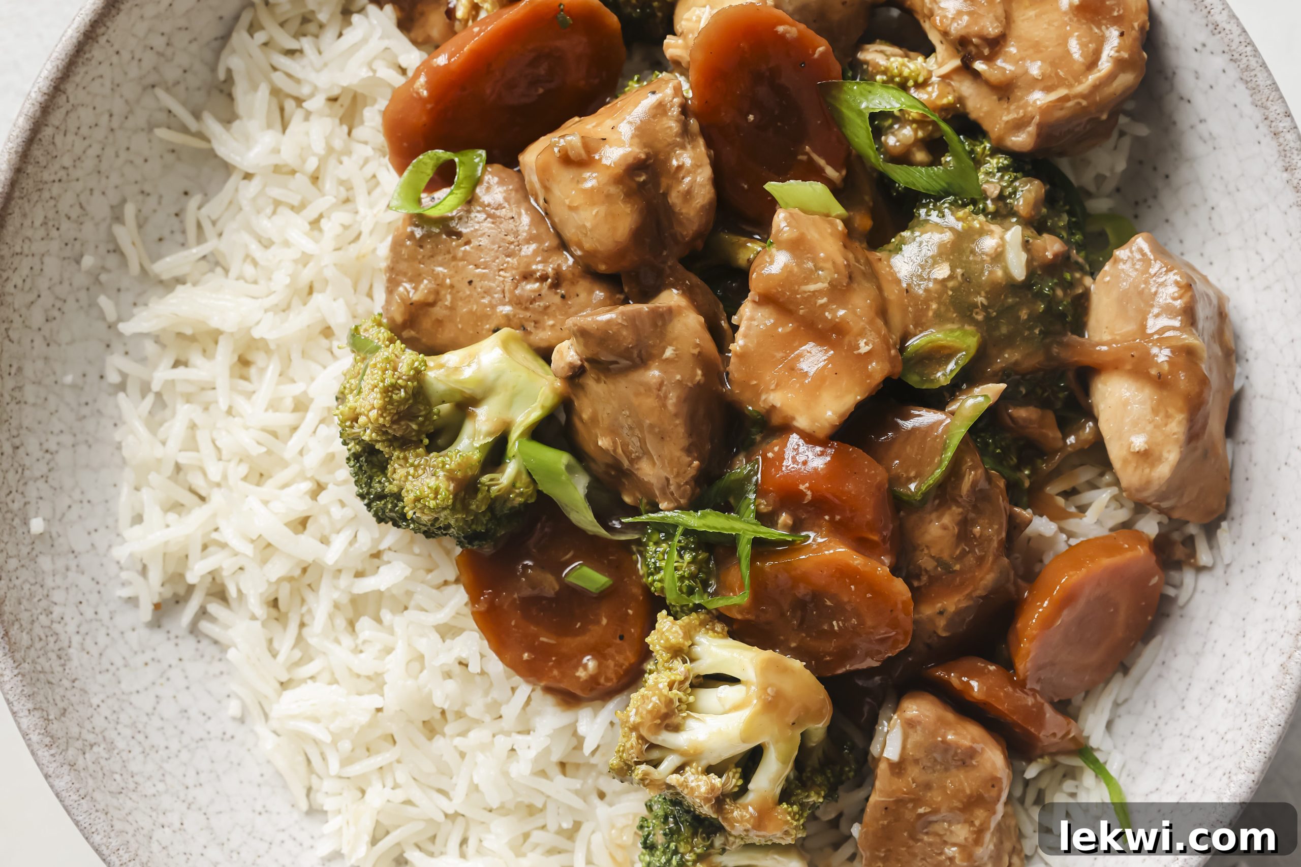 A bowl of slow cooker chicken and broccoli, served alongside a portion of rice, generously topped with freshly chopped green onions, ready to be enjoyed.