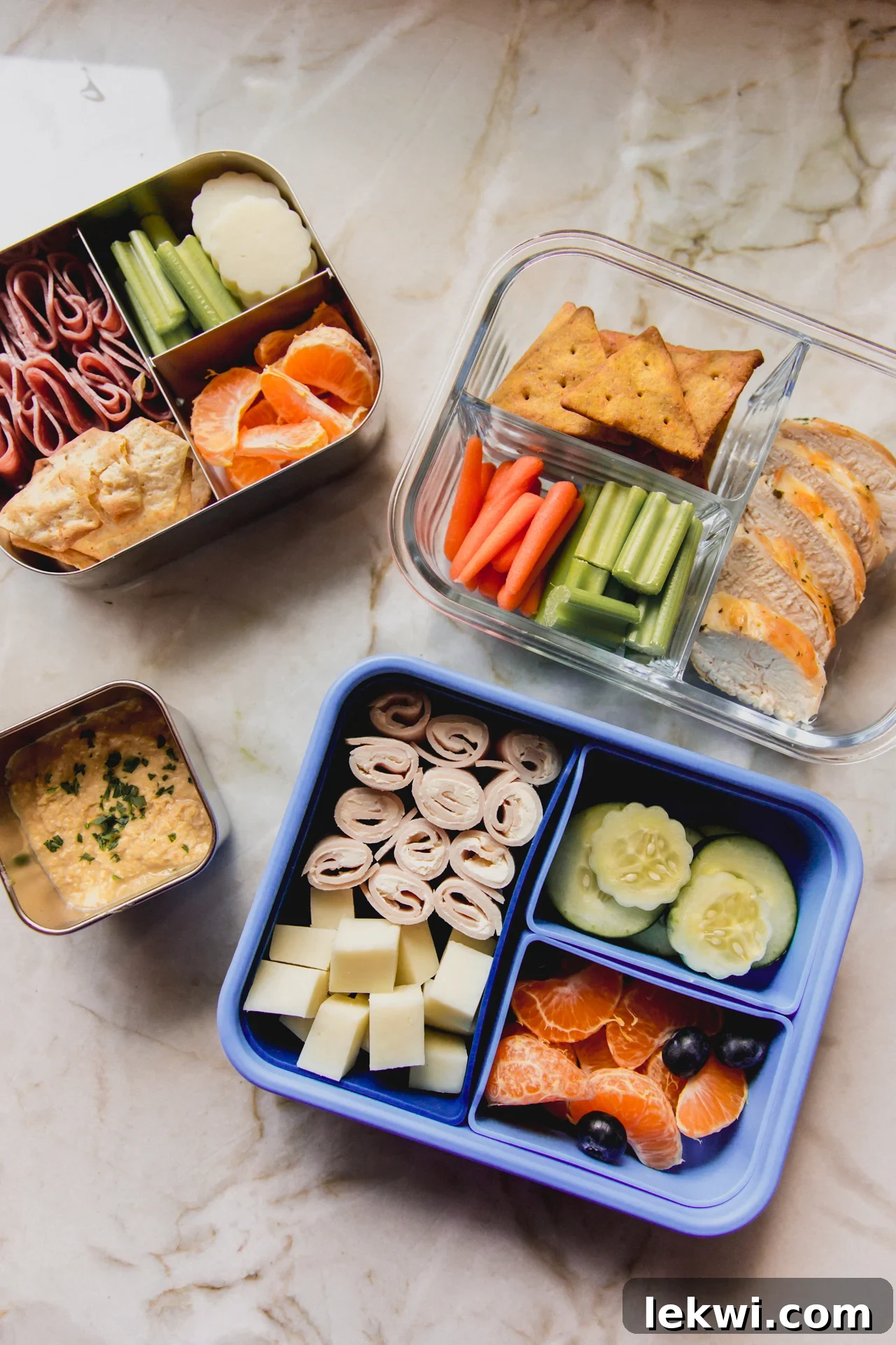 Three fully prepared kids lunch boxes with a side of hummus in a separate container.