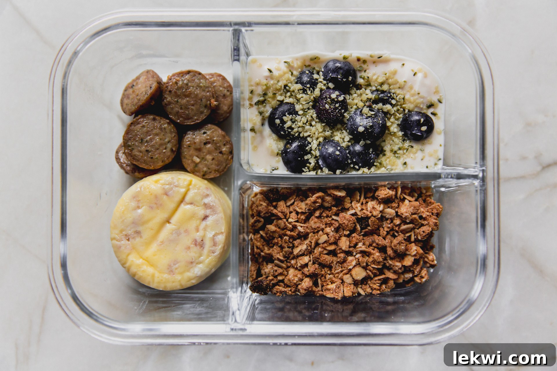 Clear divided lunch container with sausage, egg, granola, and yogurt.
