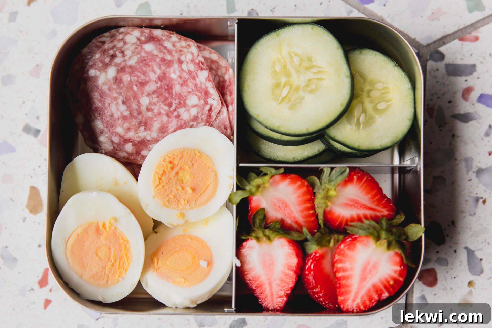 Divided lunch container with lunch meat, sliced boiled eggs, sliced cucumber, and sliced strawberries. 