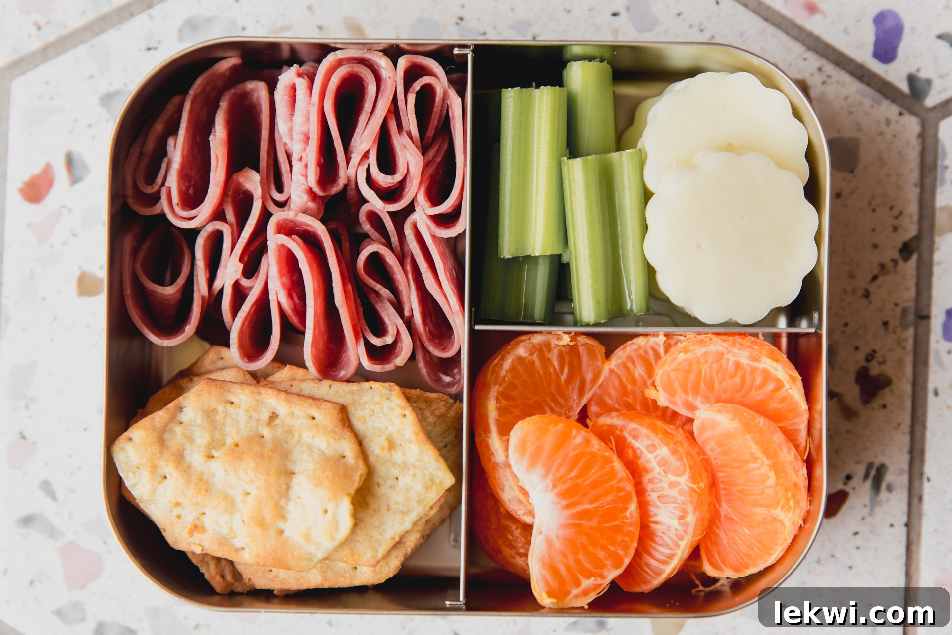 Stainless steel divided lunch container with cheese, celery, segmented clementine, lunch meat, and crackers. 
