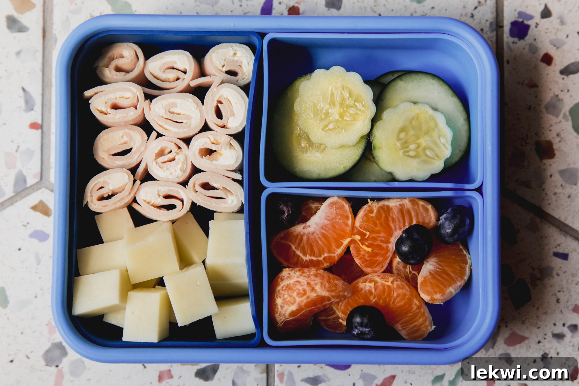Blue divided lunch container with turkey roll ups, cubed cheese, sliced cucumber, clementines and blueberries. 