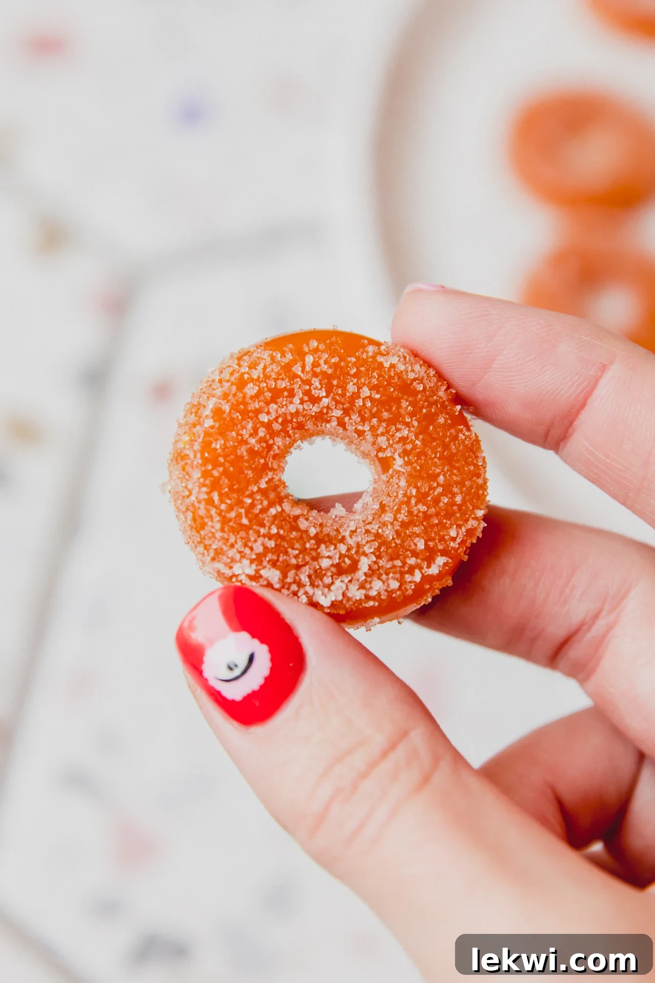 A vibrant homemade protein peach ring, perfectly chewy and sweet, held up against a blurred background, highlighting its inviting texture and color.