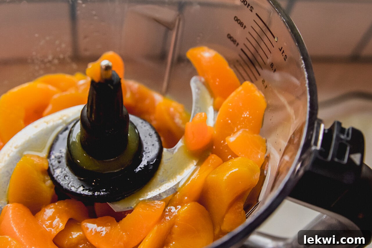 Freshly sliced peaches, vibrant orange in color, are ready to be blended with orange juice in a food processor.