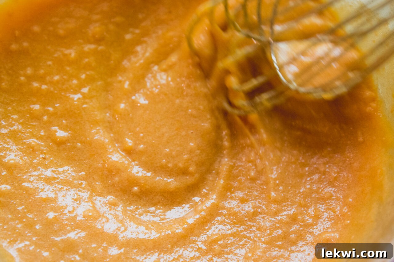 A whisk vigorously mixes the peach mixture with honey, gelatin, and unflavored protein powder in a pot, creating a smooth, thickened base for the peach rings.