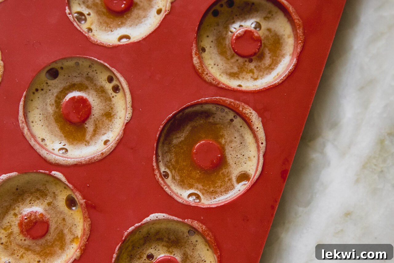 Liquid protein peach ring mixture has been carefully piped into a red, ring-shaped silicone gummy mold, ready for chilling.