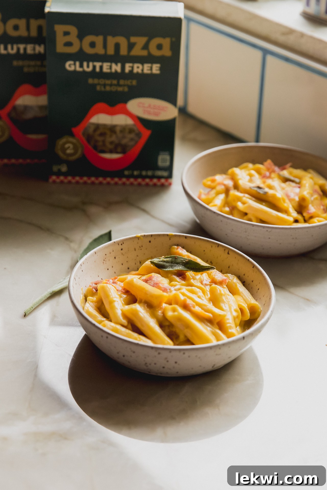 Two bowls of creamy butternut squash pasta bake, garnished with fresh sage leaves and crispy prosciutto, set on a rustic wooden surface, embodying cozy autumn comfort food.