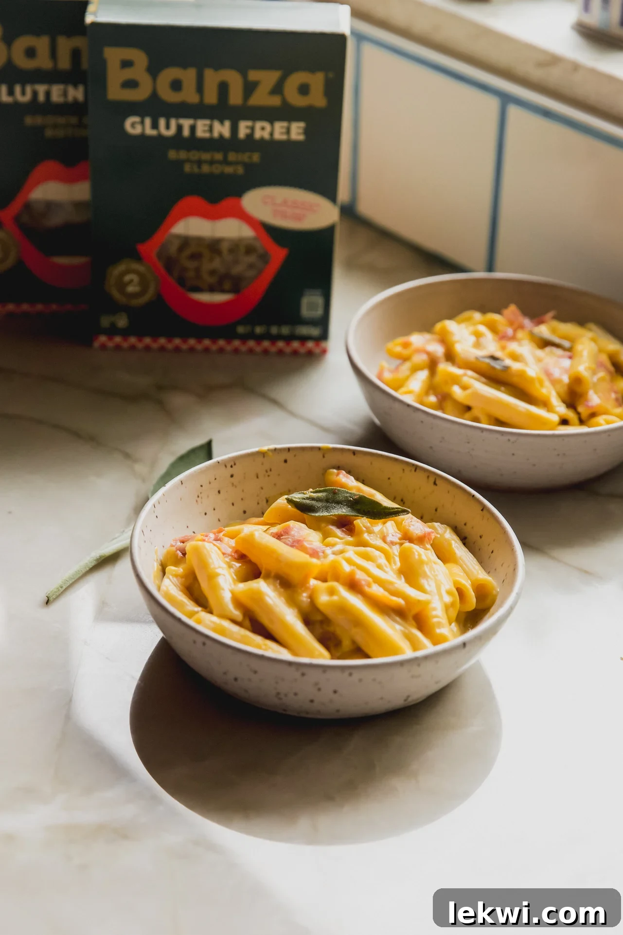 Creamy butternut squash pasta bake in separate bowls, garnished with fresh sage and crispy prosciutto.
