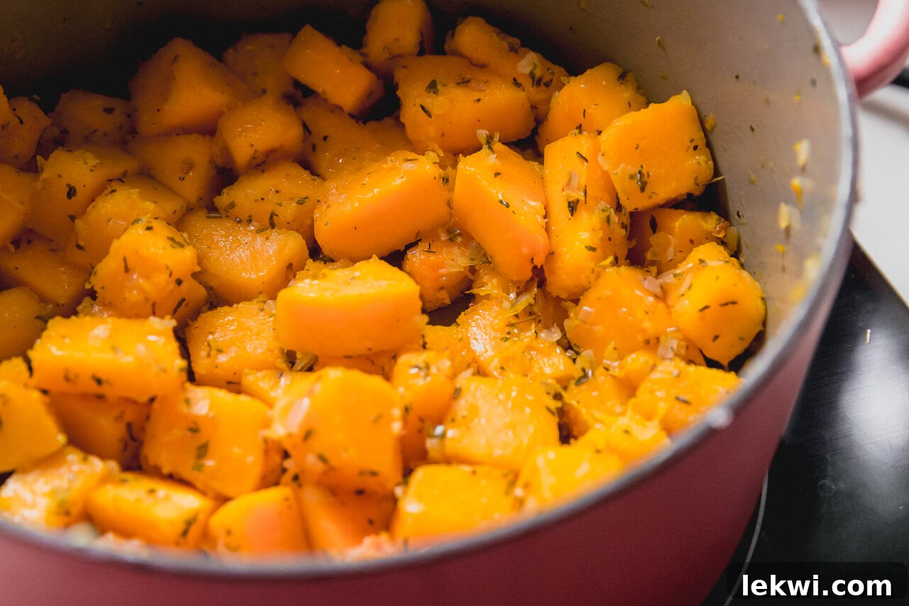 Cubed butternut squash, diced shallots, and minced garlic sautéing in avocado oil in a Dutch oven, releasing fragrant aromas.