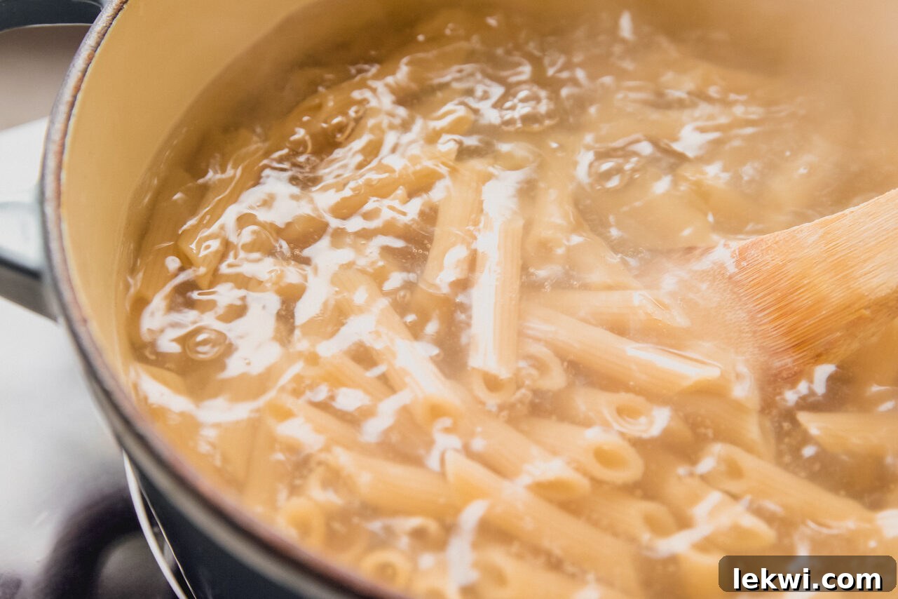 Banza brown rice pasta boiling in a pot of salted water on a stovetop, preparing for the bake.