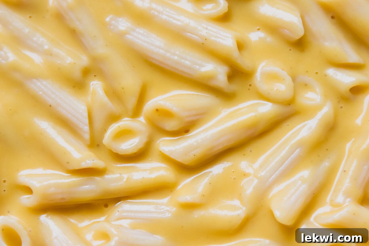 Gluten-free pasta combined with creamy butternut squash sauce in a glass baking dish, topped with shredded goat mozzarella, ready for broiling.